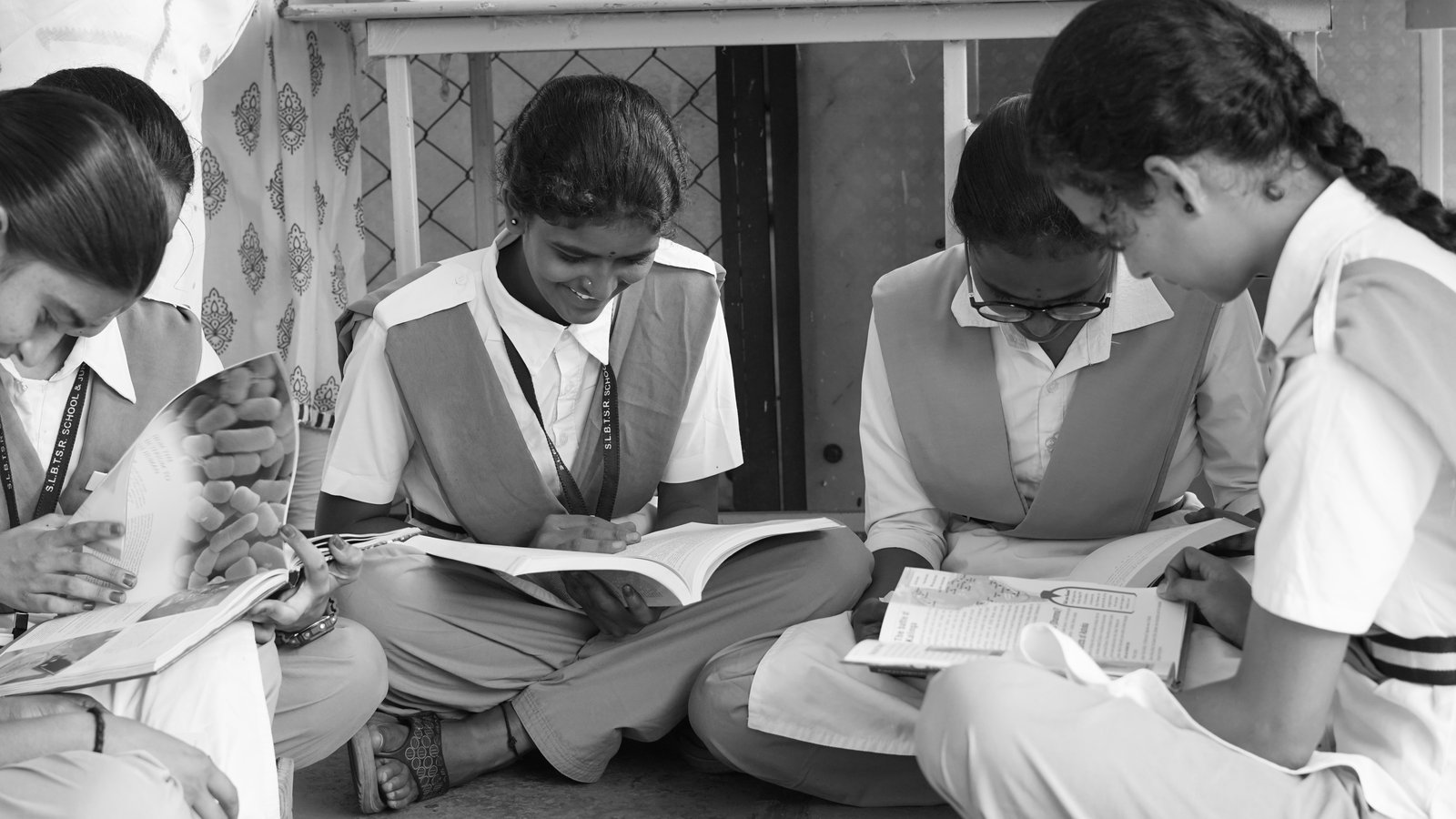 A group of school students in uniform sitting together, absorbed in reading textbooks.